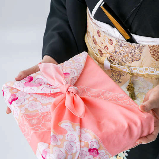 A Japanese woman holing a beutifully wrapped gift in a traditional furoshiki fabric gift wrap
